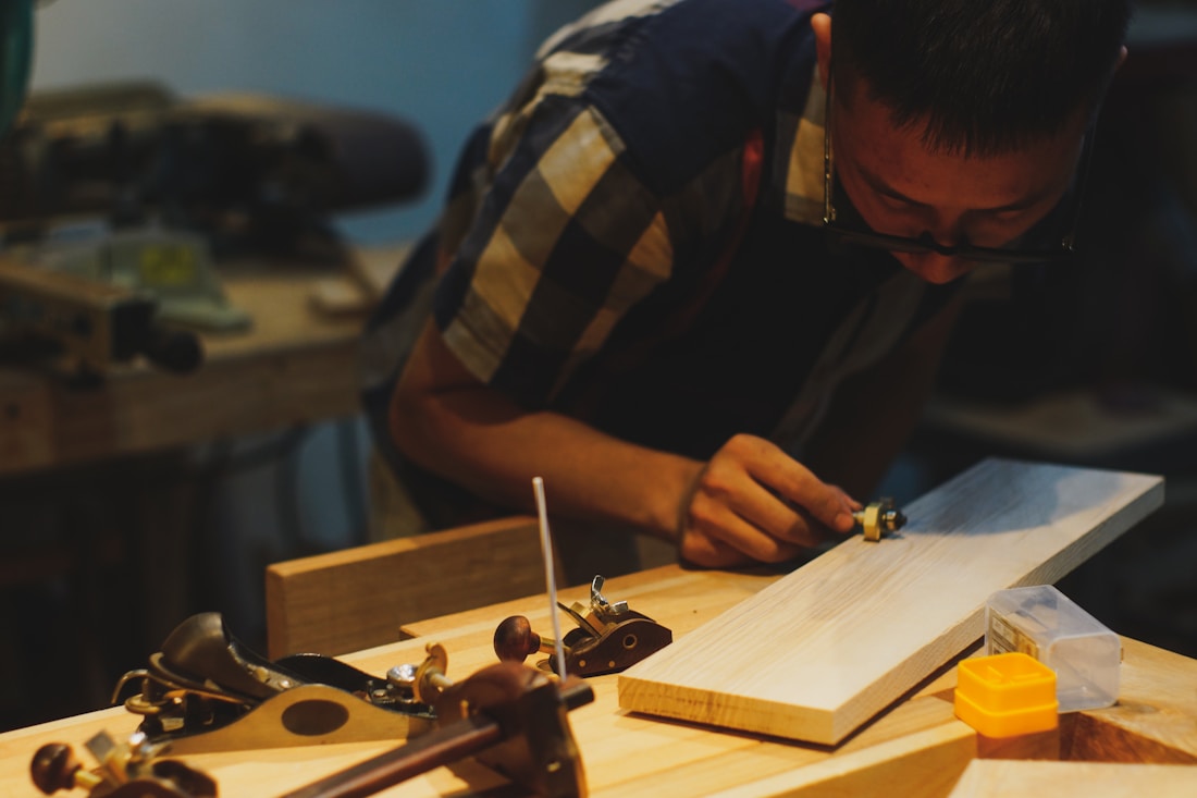 A maker marking out a board at the bench with hand planes laid out beside him